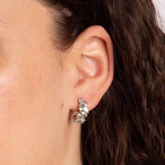 Close-up of an ear wearing a diamond earring with dark hair in the background